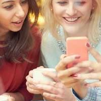 Two young women smiling while scrolling through social media on cellphone